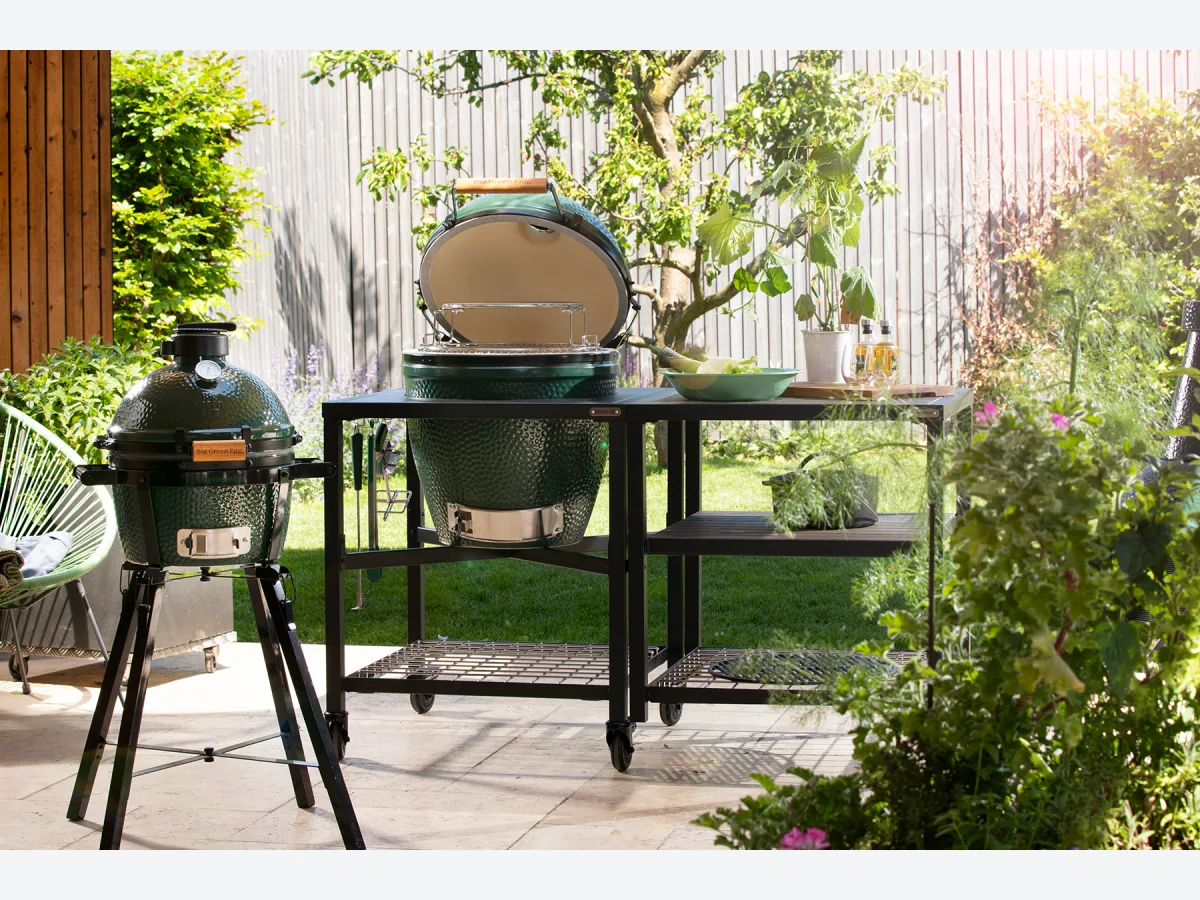 Big Green Egg Modular EGG Workspace, EGG Frame en Expansion Frame met Big Green Egg met open deksel in een tuin, met een Minimax op standaard ernaast