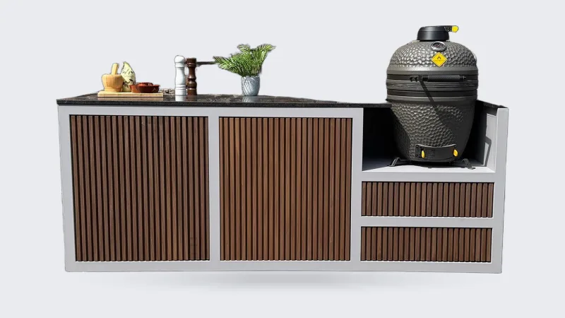 HoutenmeubelsXL Bandung, Buitenkeuken Bandung van thermohout met grijs stalen frame en natuurstenen blad, met kamado rechts, recht van voren voor een bakstenen muur