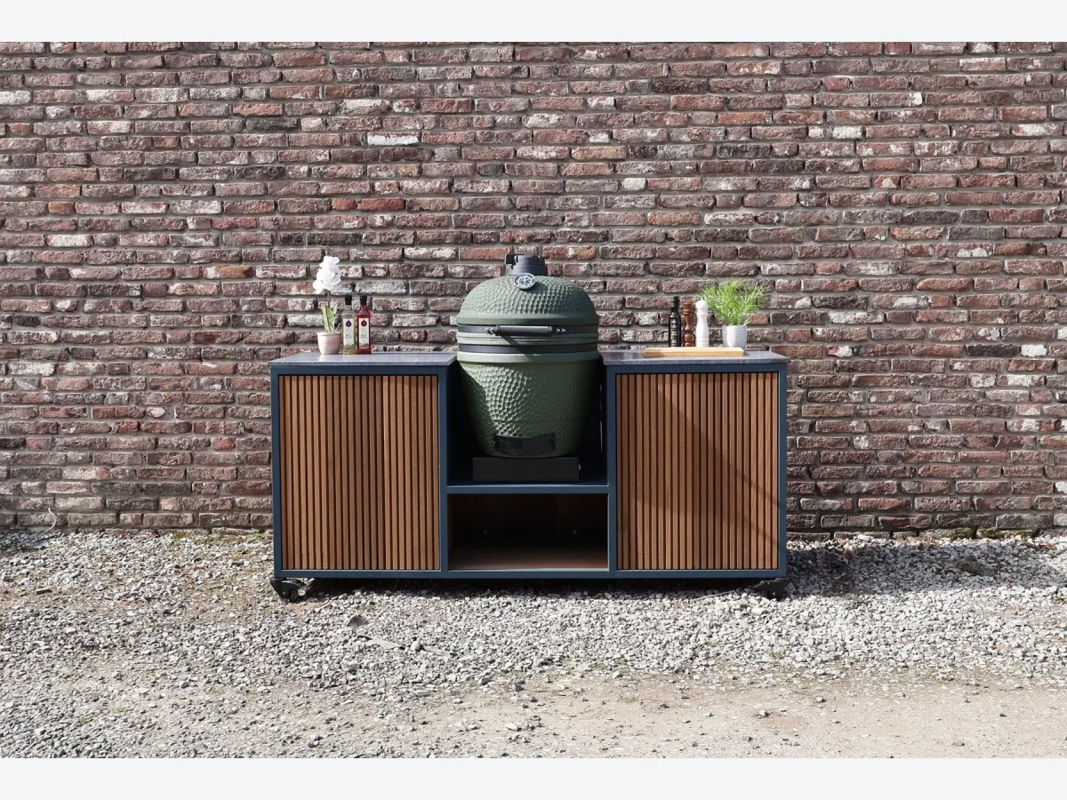 HoutenmeubelsXL Moddern, Buitenkeuken Moddern van thermohout met antraciet stalen frame en de meegeleverde Moddern kamado in het middenvak, recht van voren voor een bakstenen muur