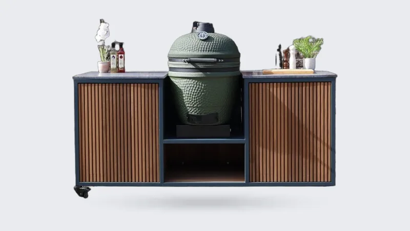 HoutenmeubelsXL Moddern, Buitenkeuken Moddern van thermohout met antraciet stalen frame en de meegeleverde Moddern kamado in het middenvak, recht van voren voor een bakstenen muur