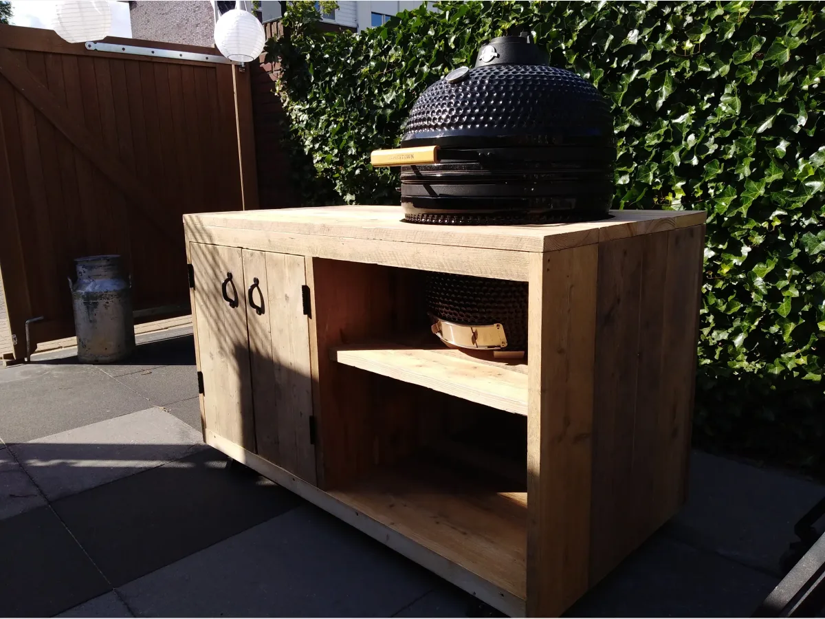 Maison DAM Op maat, Buitenkeuken op maat van steigerhout met zwarte kamado en open vak, driekwart van linksvoor voor een haag