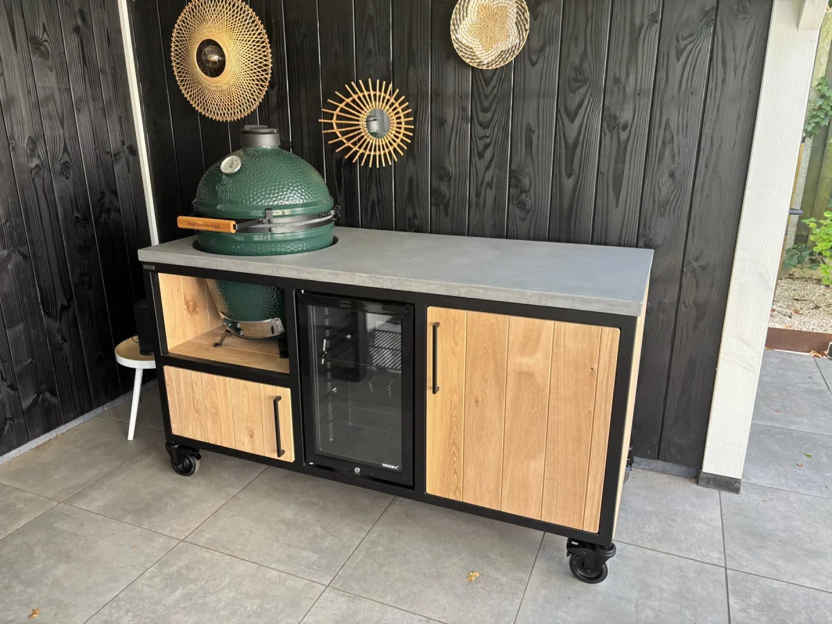 MB Industrial Living Basic, Buitenkeuken Basic met Big Green Egg links, inbouwkoelkast en houten deur, recht van voren voor een zwarte houten wand