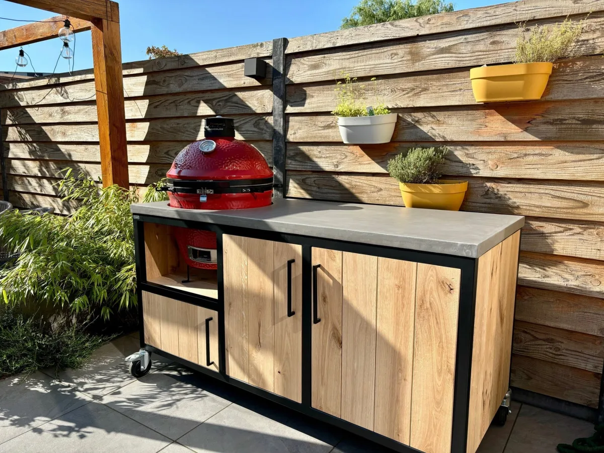 MB Industrial Living Basic, Buitenkeuken Basic met rode kamado links en twee houten deuren, voor een houten schutting met plantenbakken