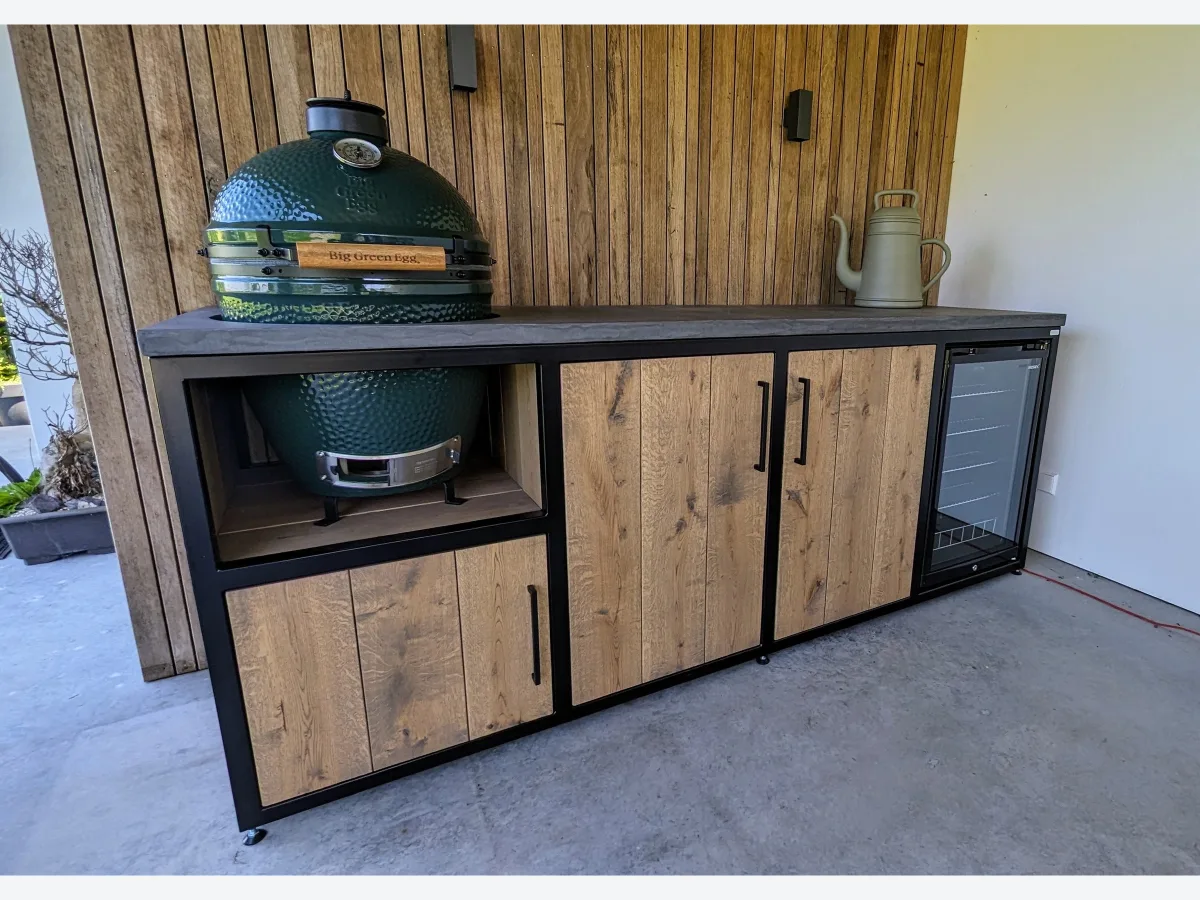 MB Industrial Living Maatwerk buitenkeuken, Maatwerk buitenkeuken met Big Green Egg links, eiken deuren en inbouwkoelkast, voor een wand van houten latten