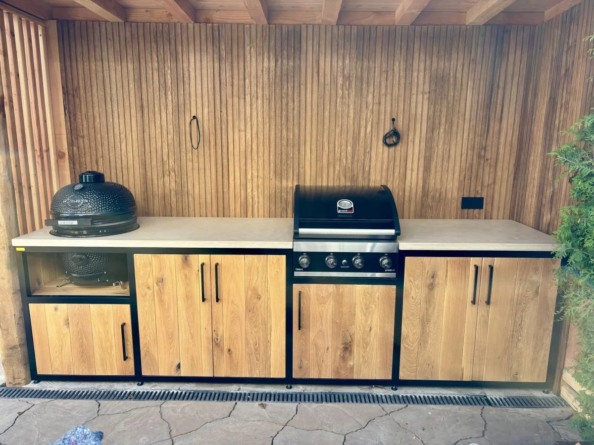 MB Industrial Living Maatwerk buitenkeuken, Maatwerk buitenkeuken met kamado links en gasbarbecue in het midden, eiken deuren, voor een wand van houten latten