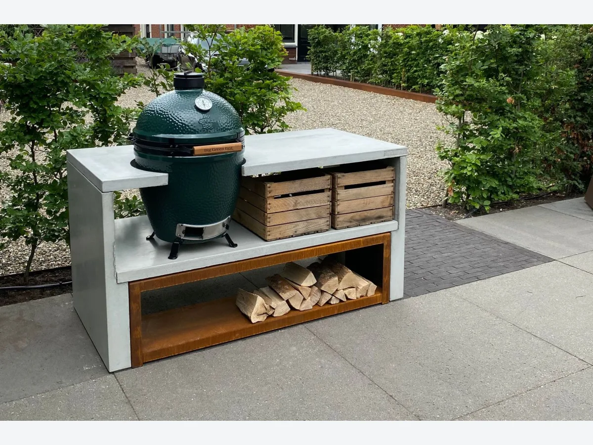 STEGG STEGG buitenkeuken, Grijze STEGG buitenkeuken met Big Green Egg, kratten en cortenstalen houtopslag op een terras met grind en hagen