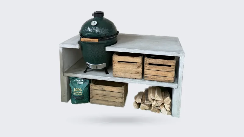STEGG STEGG buitenkeuken, Vrijstaande foto van de grijze betonnen STEGG buitenkeuken met Big Green Egg, houten kratten en haardhout, driekwart van linksvoor op transparante achtergrond
