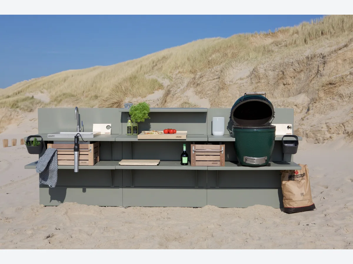 WWOO Staal, WWOO stalen buitenkeuken in olijfgroen met geopende Big Green Egg, spoelbak en houten kratten, op het strand voor de duinen