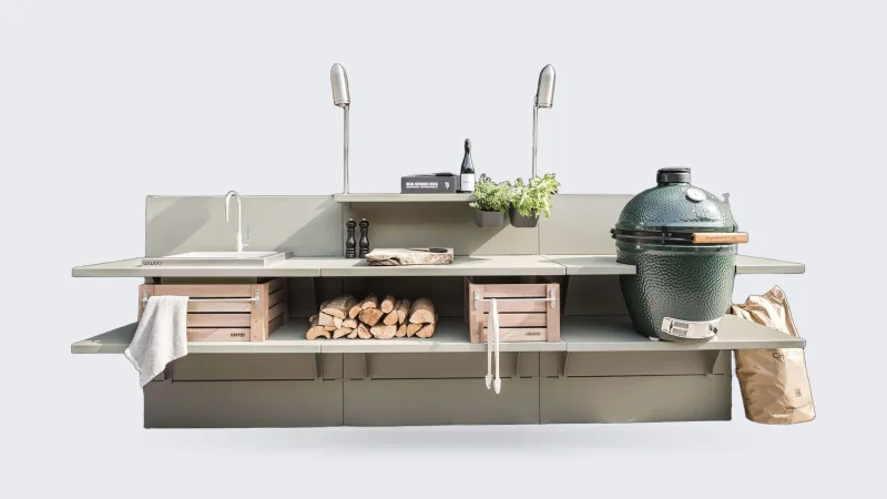 WWOO Staal, WWOO stalen buitenkeuken in groen met spoelbak, haardhout, houten kratten en Big Green Egg, tegen een zwarte houten schuur